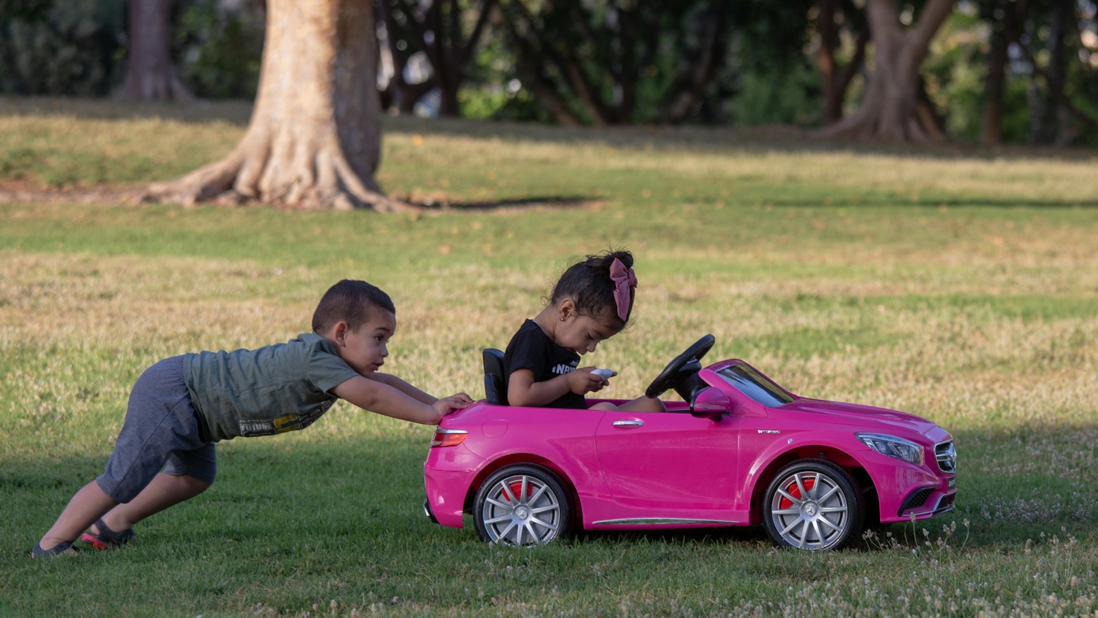 two children playing with a pink toy car