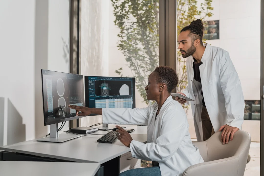 Two medical professionals in white coats reviewing a brain scan on computer monitors