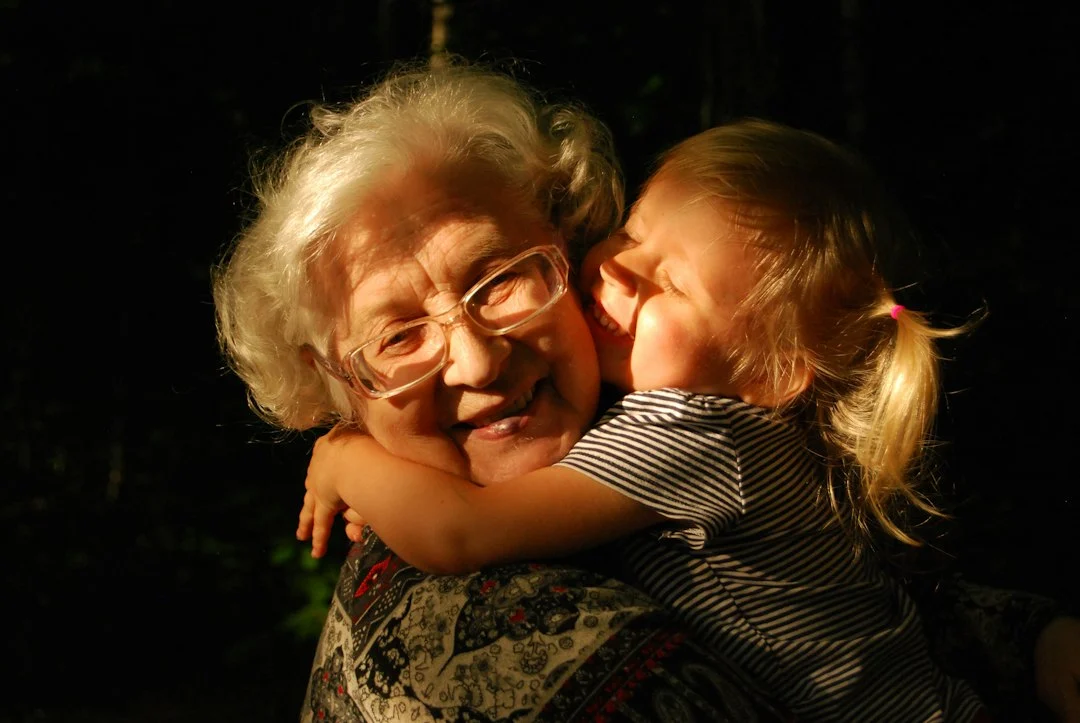 An elderly woman with white hair and glasses hugging a young child