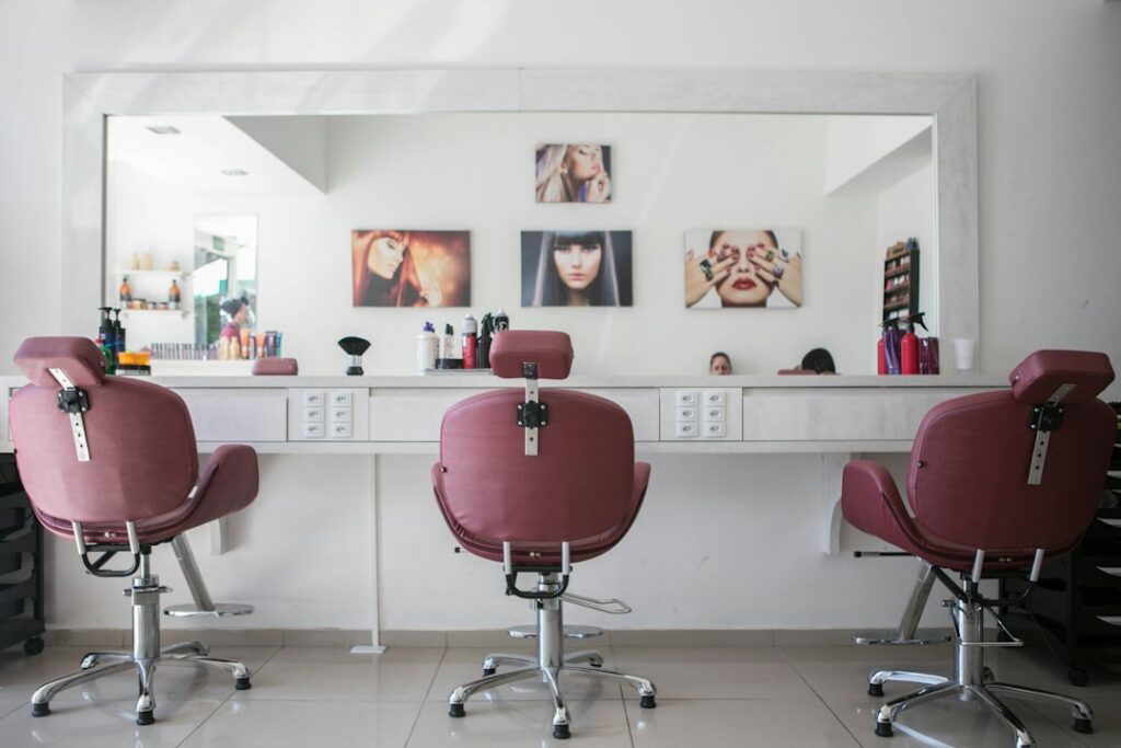 Three maroon salon chairs facing a long white counter with a large mirror