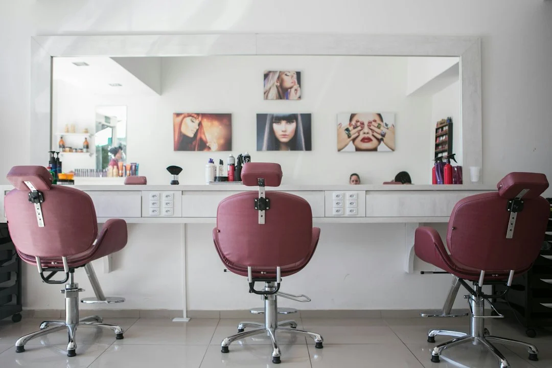 Three maroon salon chairs facing a long white counter with a large mirror
