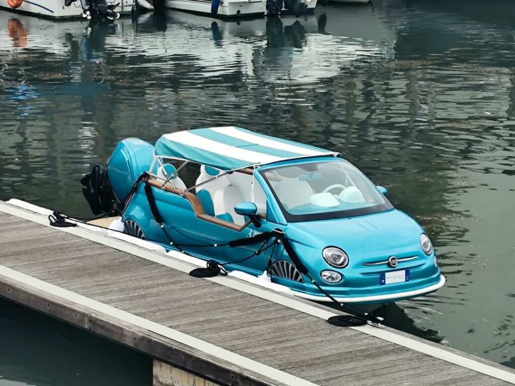 A turquoise Fiat 500 car boat with a striped canopy moored at a dock