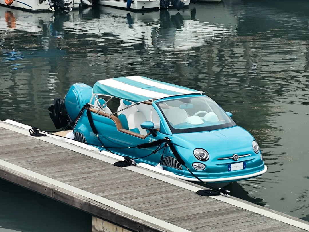 A turquoise Fiat 500 car boat with a striped canopy moored at a dock