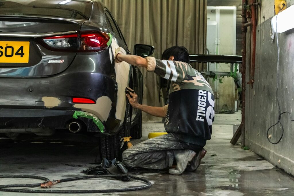 A person sanding the body of a grey car in an auto repair shop