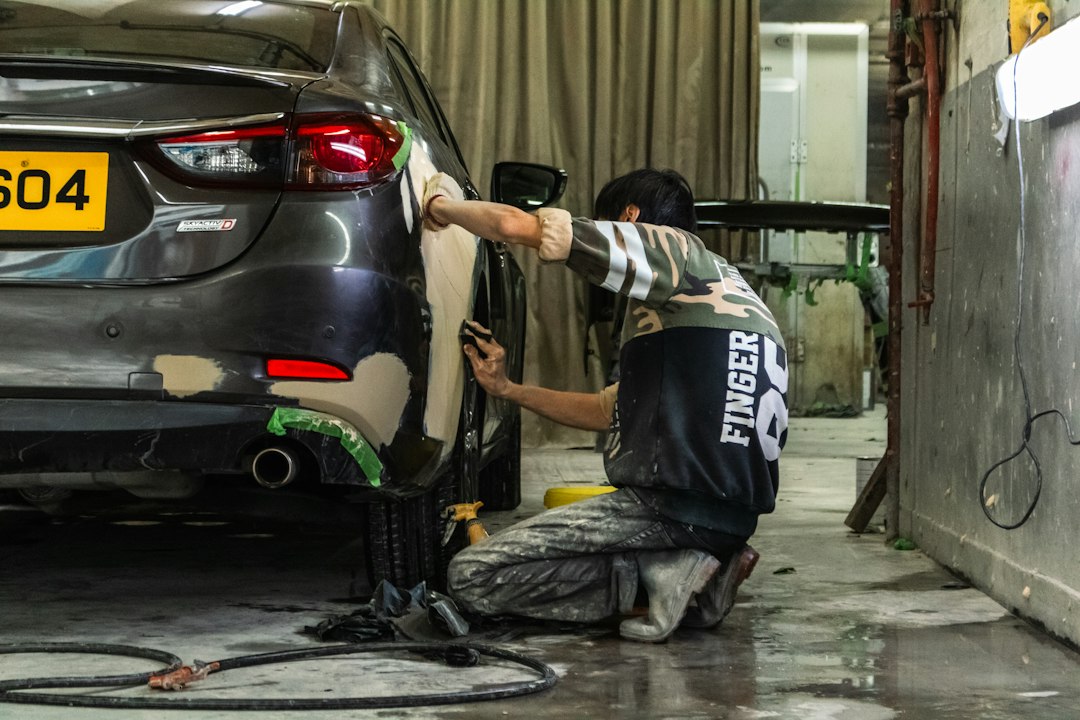 A person sanding the body of a grey car in an auto repair shop