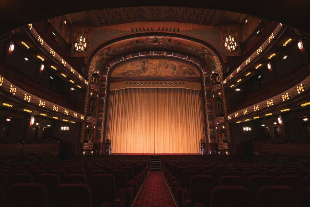 An empty theater with rows of red seats facing a closed gold curtain
