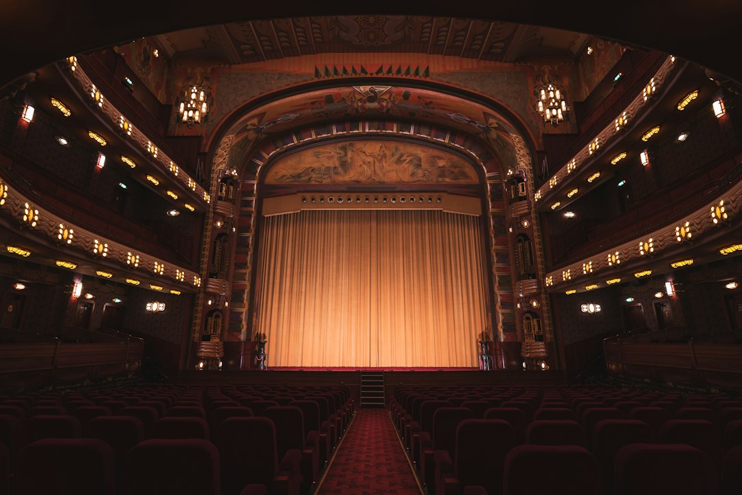 An empty theater with rows of red seats facing a closed gold curtain