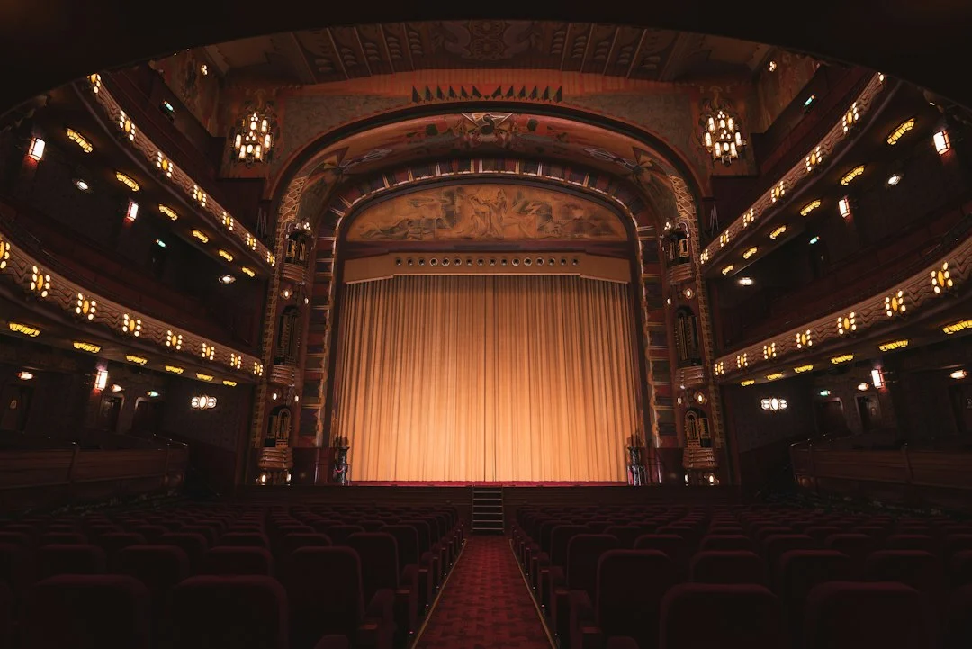 An empty theater with rows of red seats facing a closed gold curtain